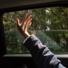 a person's hand out the window of a car with trees in the background