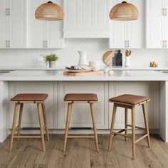 two wooden stools sit in front of an island with white cabinets and countertops