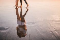 two people walking on the beach with their reflection in the wet sand