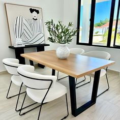 a dining room table with white chairs and a vase on it's end, in front of a large window