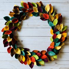 a wreath made out of felt leaves sitting on top of a white wooden table next to a wall