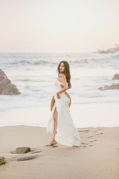 a woman standing on top of a sandy beach next to the ocean wearing a white dress