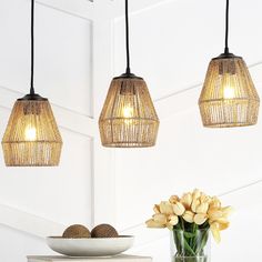 three lights hanging from the ceiling over a table with flowers in a vase and bowl