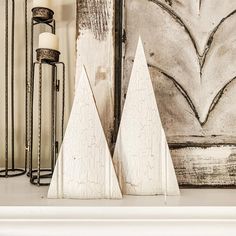 two white wooden christmas trees sitting on top of a mantle next to a lit candle