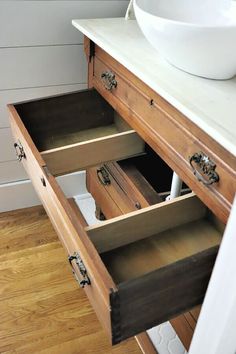 an open drawer in a bathroom with a bowl on the counter and wood flooring