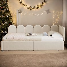 a white day bed sitting in front of a christmas tree with lights on the wall