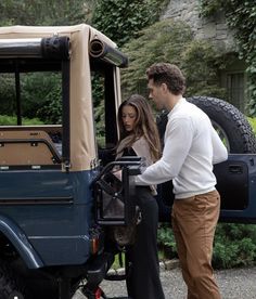 a man and woman standing in front of a blue jeep with the door open, looking at each other