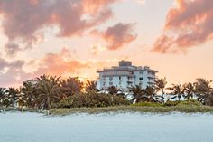 the sun is setting over an ocean with palm trees and buildings in the background,