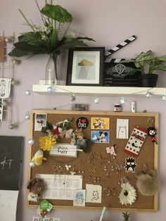 a bulletin board with flowers, pictures and other things on it next to a potted plant