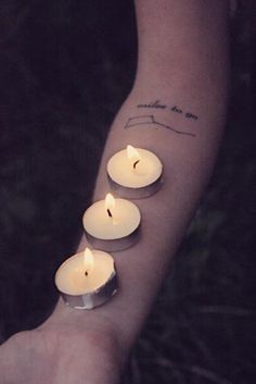 three lit candles in the palm of someone's hand with words written on it