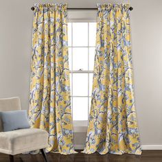 a yellow and blue floral curtain hanging in front of a window with a chair next to it