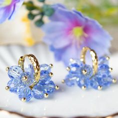 two pairs of blue earrings sitting on top of a white plate next to purple flowers