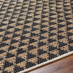 an area rug with black and tan squares on top of wooden flooring next to a wood table