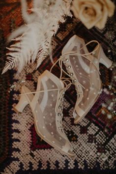 white high heeled shoes sitting on top of a rug next to feathers and flowers