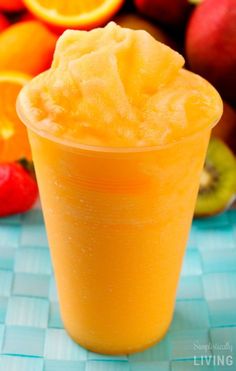 an orange smoothie in a plastic cup next to fresh fruit on a tablecloth