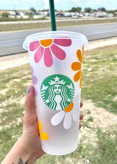 a hand holding up a starbucks cup with flowers on it and a green plastic straw