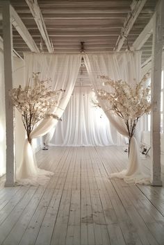 an empty room with white drapes and flowers