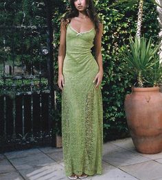 a woman in a long green dress standing next to a potted plant and looking at the camera