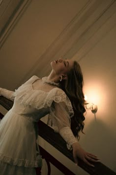 a woman in a white dress is standing on a stair railing and looking up at the ceiling