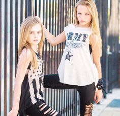 two beautiful young women standing next to each other near a metal fence, one in black and the other in white