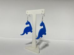 a pair of earrings with blue dinosaur silhouettes hanging from it's ear hooks