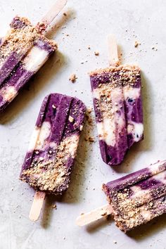 three popsicles with blueberries and crumbled toppings sitting on a white surface