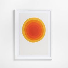 an orange and yellow circle on a white background in a square frame hanging on the wall