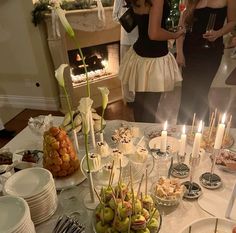 a table filled with food and candles in front of people standing around the table at a party