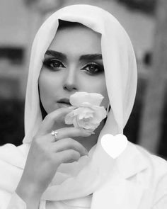 a woman wearing a white hijab and holding a rose in her hand with a heart on it