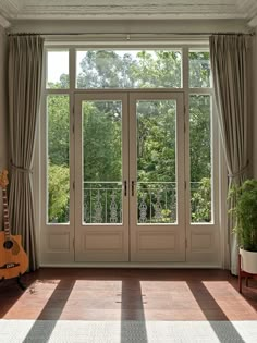 a guitar is sitting on the floor in front of a window with curtains and drapes