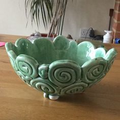 a green bowl sitting on top of a wooden table next to a potted plant