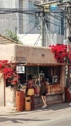 people are walking past a small store with red flowers