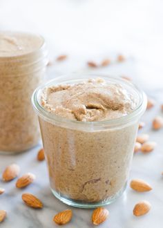 two jars filled with food sitting on top of a table next to almonds and nuts