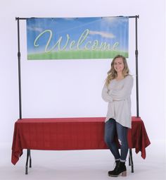 a woman standing next to a red table with a welcome sign on it's side