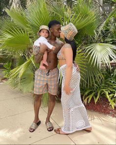 a man and woman are standing in front of palm trees while holding a small child