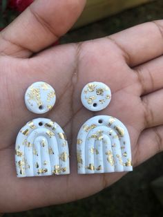 two white and gold earrings in someone's hand