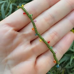 a hand holding a green beaded bracelet with multicolored beads on it's end