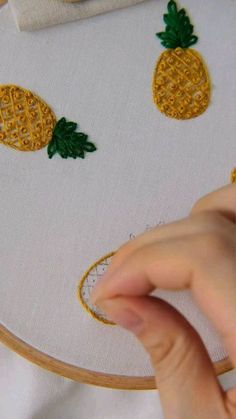 someone is stitching pineapples on a piece of white fabric with yellow thread