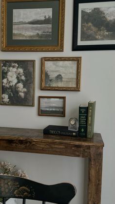 a wooden table topped with books next to pictures and framed art on the wall above it