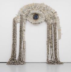 a sculpture made out of beads and chains with an eye in the center, on a white wall