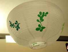 a white paper lantern with green leaves on it hanging from the ceiling in a room