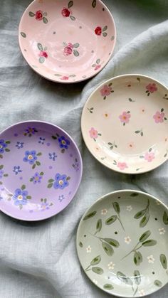 three bowls with flowers painted on them sitting on a white cloth covered tablecloth, one is empty and the other has no lid