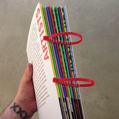 a hand holding a stack of colored pencils in it's left side, with the book open