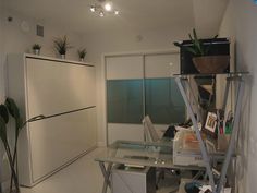 a room with a glass desk and shelves filled with plants, books, and other items