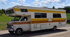 an old camper parked on the side of a road in front of a green field