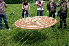 four people are standing in the grass near a large piece of art that looks like a maze