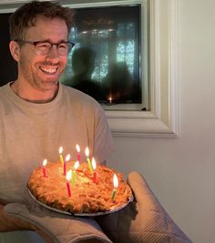 a man holding a cake with lit candles on it in front of a windowsill