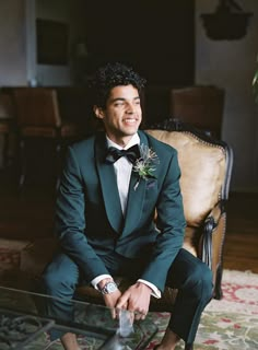 a man in a tuxedo sits on a chair and smiles at the camera