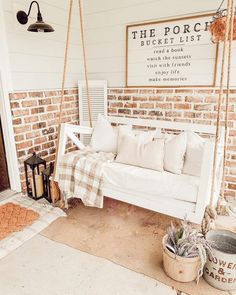 a porch swing with pillows on it next to a brick wall and potted cacti