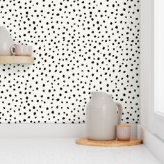 two white vases sitting on top of a counter in front of a wall with black dots